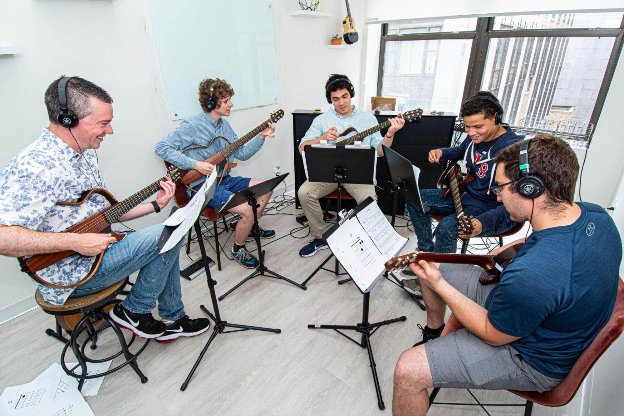 Adult music students learning acoustic guitar in group lesson at music school in Boston MA